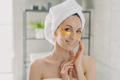 Smiling woman wearing towel using hydrogel patches on under eye skin in bathroom. Skincare routine - PhotoDune Item for Sale