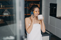 Pretty girl with under eyes patches drinks morning coffee talking by phone during skincare at home - PhotoDune Item for Sale