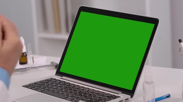 Male Doctor Treats Hands with Antiseptic and Uses Laptop with Green Screen Chroma Key for Work and