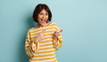 Delighted young ethnic woman pointing away and smiling in studio - PhotoDune Item for Sale