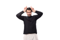 young handsome brunet european man in a black sweater builds horns on an isolated white background - PhotoDune Item for Sale