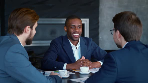 Happy african american man in suit with colleagues at the table at meeting