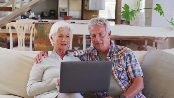 Senior caucasian couple having a video chat on laptop while sitting on couch at home