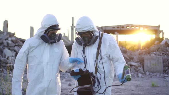 Portrait of Two Scientists in White Overalls and Protective Masks Taking Measurements of Radiation