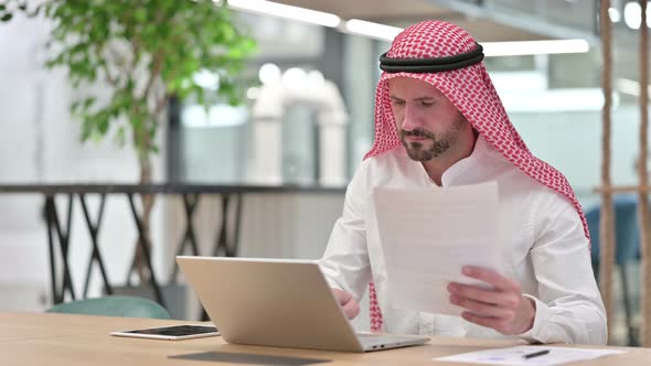 Serious Businessman Working on Laptop with Documents 