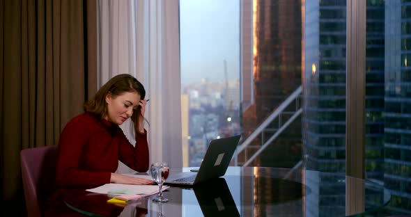 A Woman Sits in the Office of a Business Center at a Table, in Front of Her Is a Laptop, a Glass