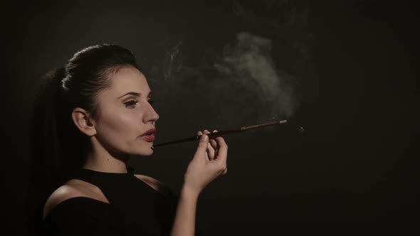 Beautiful Woman Smokes a Cigarette in a Mouthpiece on a Black Background