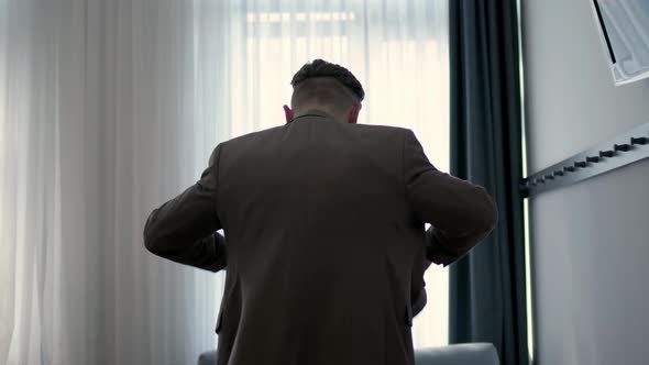 Young Businessman in Hotel Room Puts on Jacket