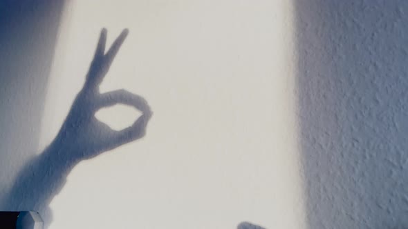 Slow motion shot of hand shadows on wall giving OK Sign during sunny day. Indoor shot on white wall