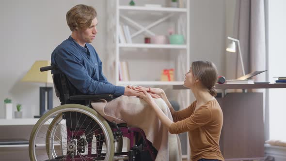 Side View Beautiful Young Woman Holding Hands of Disabled Man in Wheelchair Talking