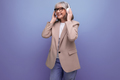 mature woman in a stylish jacket listens to music in large headphones on a bright background with - PhotoDune Item for Sale