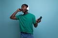 african guy in a t-shirt listens to music using headphones and smartphone - PhotoDune Item for Sale