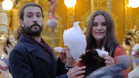 Happy carefree lovers eating cotton candy, smiling at camera-outdoor