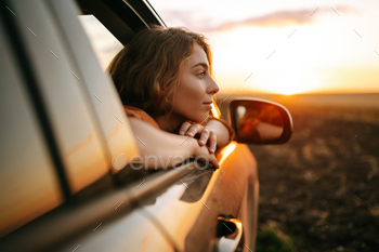 Happy woman outstretches her arms while sticking out car window. Lifestyle, travel, tourism, nature.