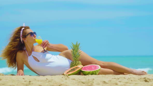 The Woman Drinks Fresh Orange Juice Background the Sea. Young Beautiful Woman Lying By the Sea on