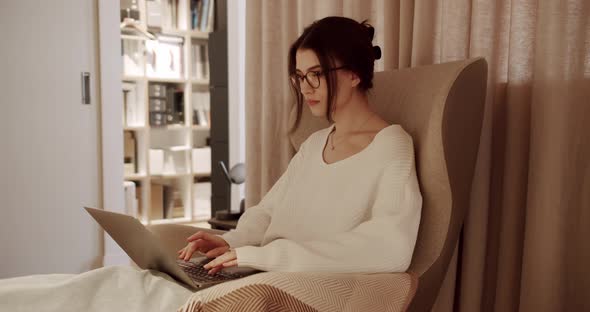 Beautiful Young Woman Works on Laptop Computer While Sitting on the Chair