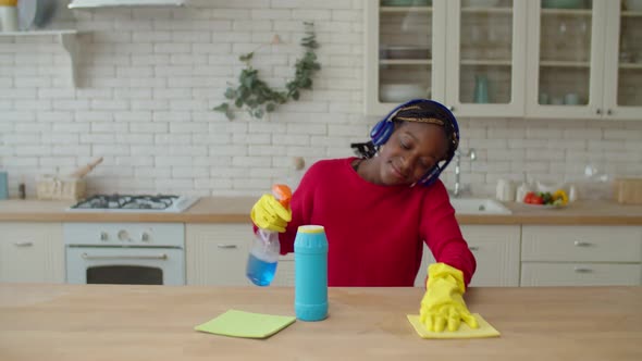 Cheerful African Teenage Girl in Headphones Cleaning in Kitchen