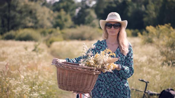 Tourist Girl Relaxing On Countryside Wildflower Field. Pretty Woman Walking With Bicycle On Field.