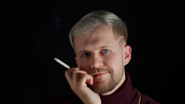 Stylish Addicted Young Man with Blue Eyes in Trendy Clothes Looking at Camera Smoking Cigarette