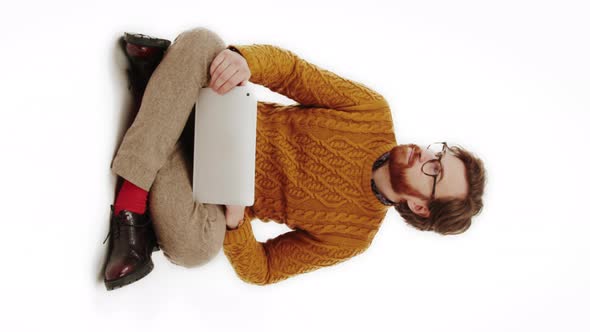 Young Man Sitting on the Floor and Working in His Laptop Full Shot Studio Shot Vertical Video White