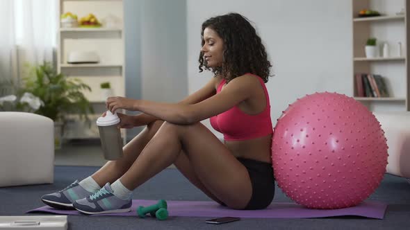 Sporty Woman Sitting on Floor in Gym Outfit and Drinking Supplement Cocktail