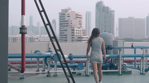 Slim Woman Walks on Hotel Blue Roof Past Colorful Pipes