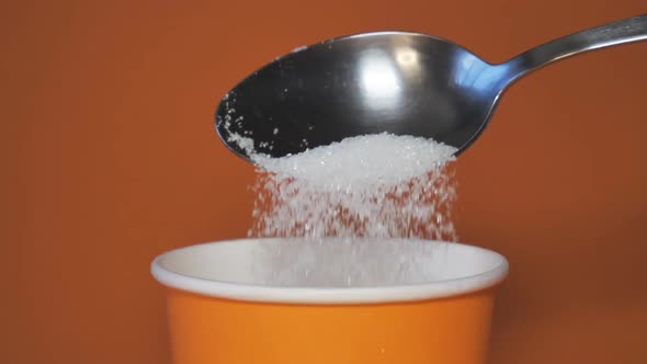 Close-up of pouring a full spoonful of white sugar crystals in slow motion. Unhealthy diet, diabetes