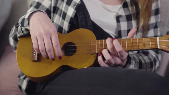 Close-up of Young Female Caucasian Hands Playing Ukulele. Teenage Girl Practicing Guitar at Home