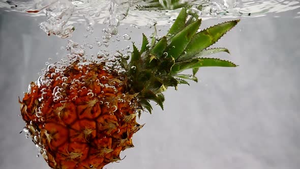 Pineapple Falls Into the Water with Splashes and Bubbles in Slow Motion.