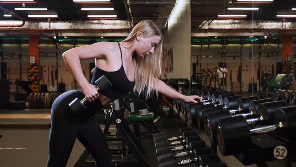 Young woman working hard in gym with dumbbell in front of the mirror to keep fit