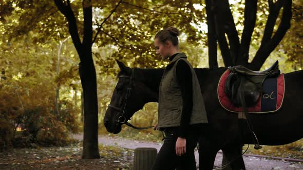 Side View of Beautiful Dark Brown Horse Walking with Young Brunette Jokey Girl in the Forest During