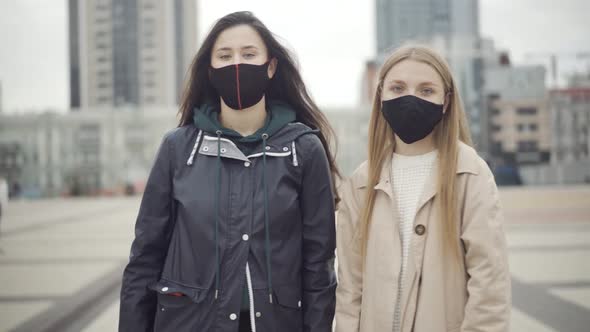 Two Confident Young Caucasian Women in Covid-19 Face Masks Turning To Camera and Showing No Gesture