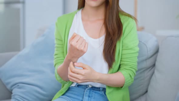 Asian young beautiful woman sitting on sofa and massage hand feel suffer from joint pain at home.