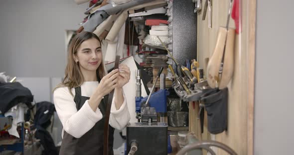 Young Woman Looking at Leather Belt in a Workshop