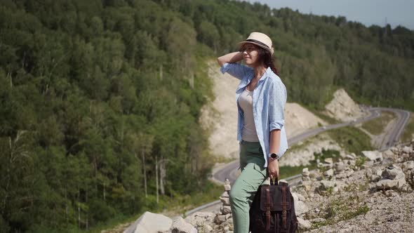 Traveler Girl Portrait in the Mountains. Young Woman with a Backpack Enjoys the View of the