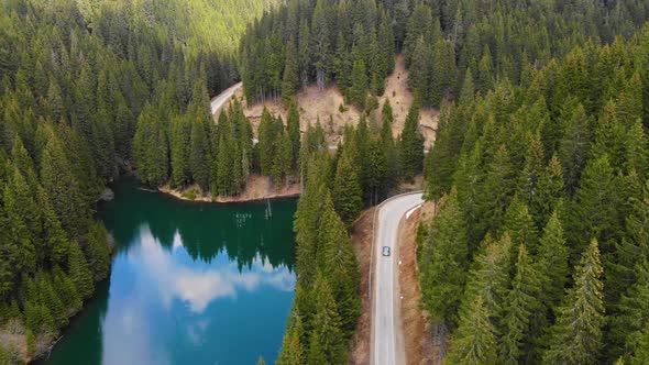 Aerial view of car driving through the forest and the lake on the side. Beautiful mountain road.