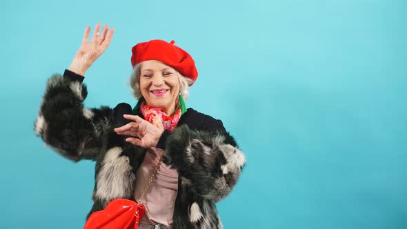 Smiling Cheerful Older Lady Dances and Looks at the Camera. Isolated Yellow Background.