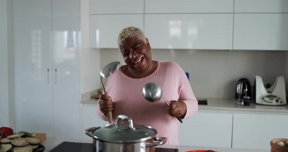 Happy black mature woman having fun cooking and dancing inside kitchen at home