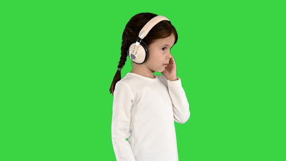 Cute Girl Dressed in White Holding Headphones with One Hand and Nodding Her Head To the Music on a