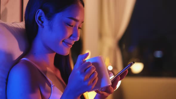 Young Asian beautiful woman enjoy using smartphone in bedroom at night time.
