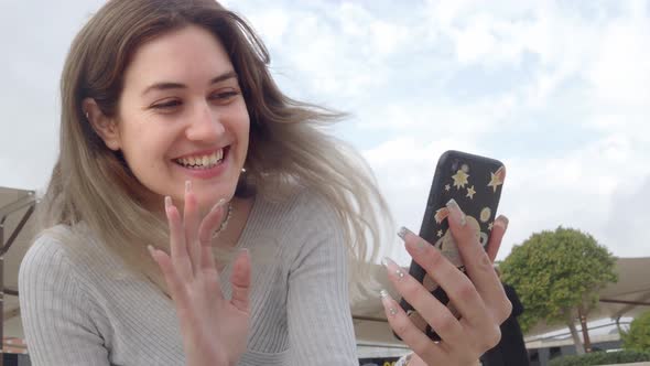 Caucasian Young Woman Making a Video Call with a Mobile Phone on the Street