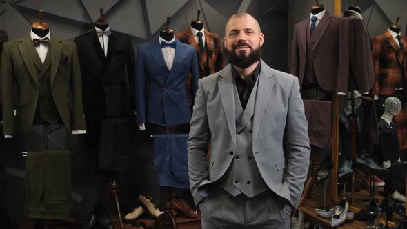 A Successful Businessman with a Beard Stands in an Atelier in a Classic Suit and Smiles. Satisfied