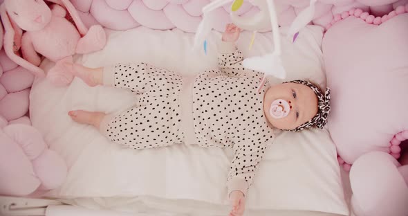 A Tiny Newborn Girl Lies In A Cradle And Looks At Toys