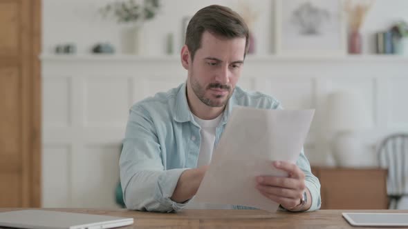 Young Man Reading Reports While Sitting in Office