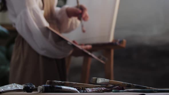 Young Woman Artist Mixing Colors on the Palette  Falling Brushes on the Foreground