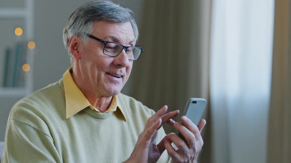 Excited Middle Aged Retired Man with Glasses Holding Telephone Make Online Shopping Communicates