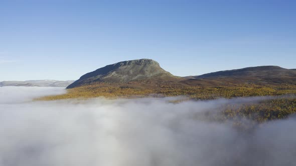 Thick mist and foggy landscape during a sunny day filmed from air with rocky mountain in the backgro