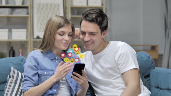 Smiling Young Couple Using Smartphone Flying Smileys Emojis and Likes