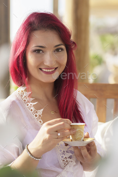 girl with red hair gown on a summer terrace among plants laughs drinks coffee,resting,morning coffee