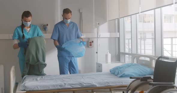 Nurses in Safety Mask and Gloves Making the Bed and Changing Sheets in Hospital Ward